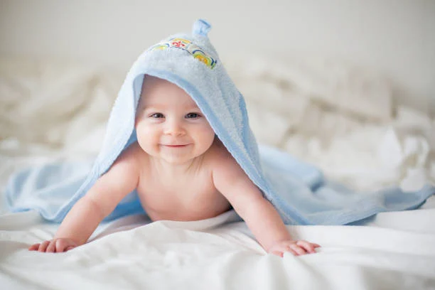 smiling baby wrapped in a blue towel, crawling on a soft white bedspread