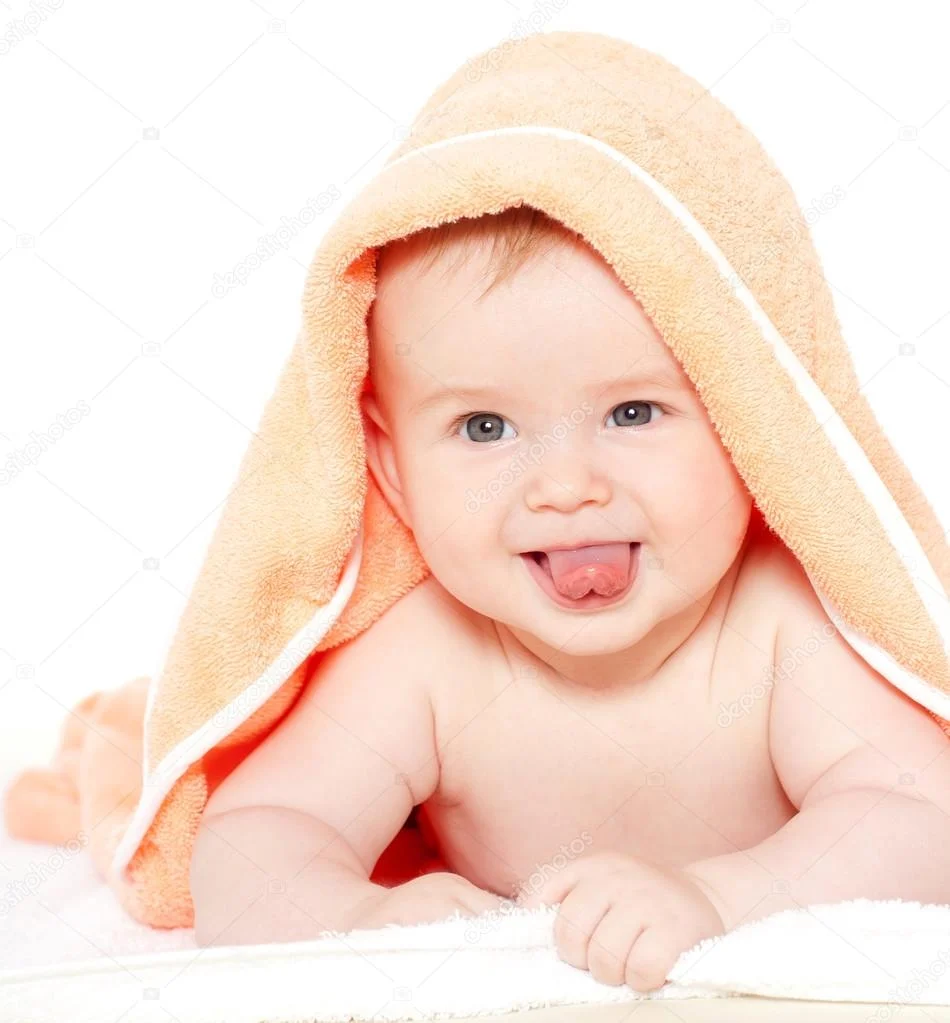 smiling baby with blue eyes and a towel on their head, playfully sticking out their tongue