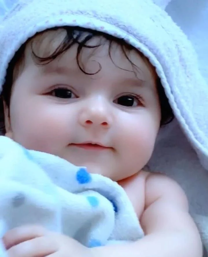 adorable baby with curly hair wrapped in a towel, smiling softly at the camera