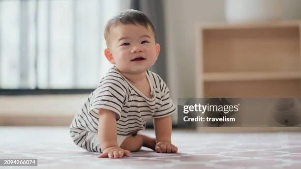 smiling baby boy in striped outfit sitting on a patterned rug indoors