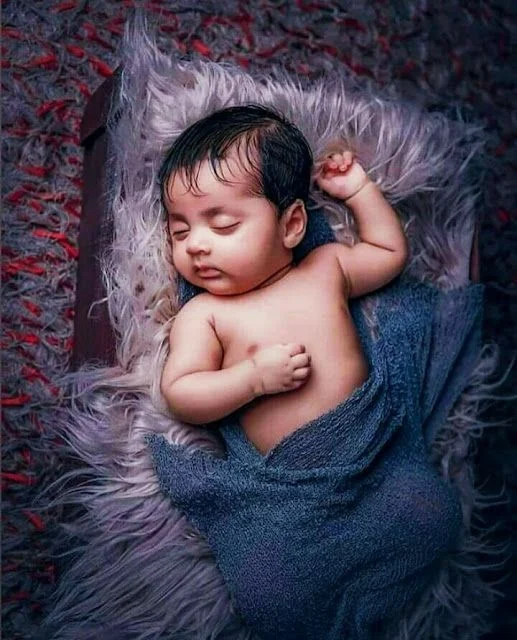 sleeping baby wrapped in a blue blanket on a fluffy surface, with a peaceful expression and slightly curled fingers