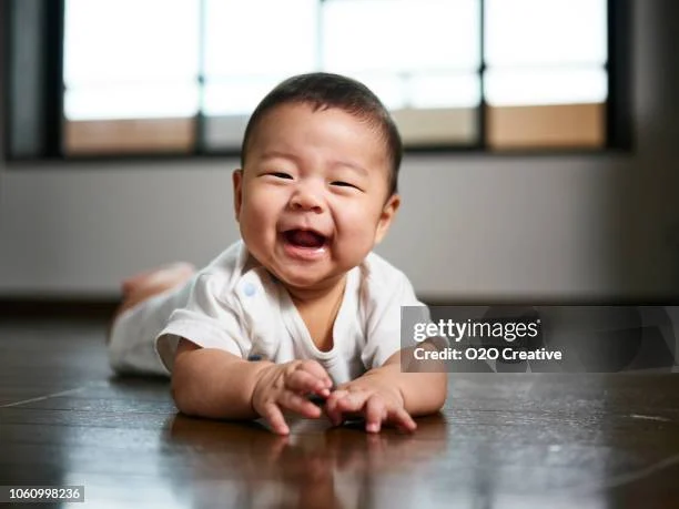 happy baby lying on the floor, smiling widely with hands outstretched, bright natural light in the background