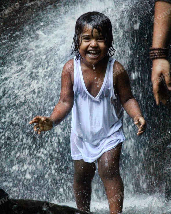 laughing child in a white shirt playing joyfully under a waterfall, surrounded by splashes of water