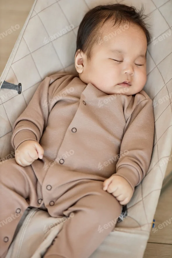 cute baby boy sleeping in a beige onesie, resting comfortably in a soft, cushioned chair