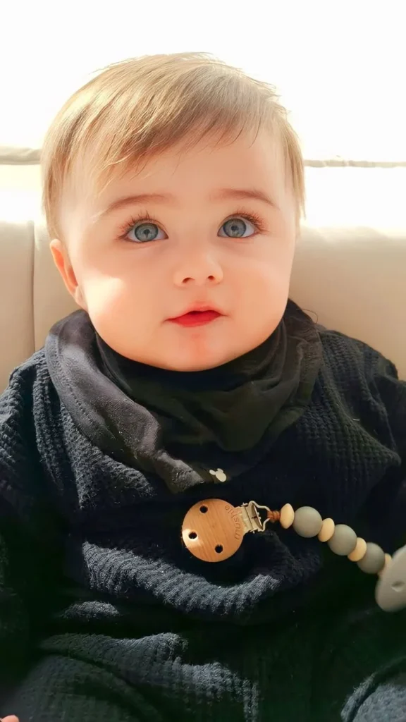 cute baby with blue eyes and light brown hair, wearing a black outfit and a pacifier clip, sitting indoors